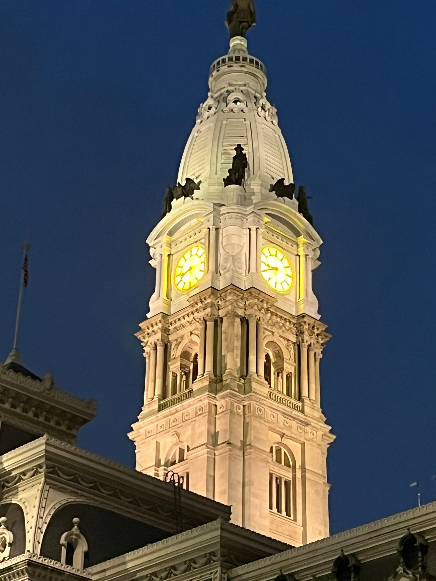 Philadelphia City Hall’s clock tower at night. The clock panel itself is lit up in a bright yellow with the numbers being repersented by roman numerals.